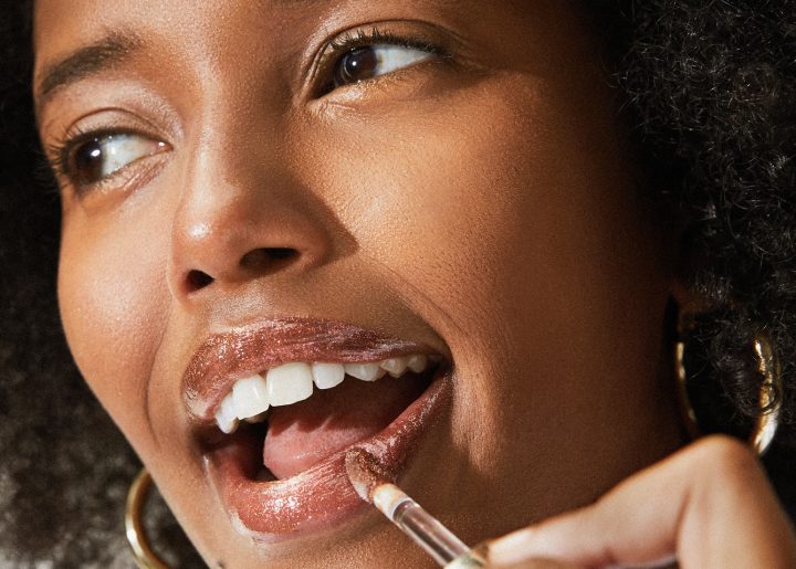 Black woman applying lip gloss