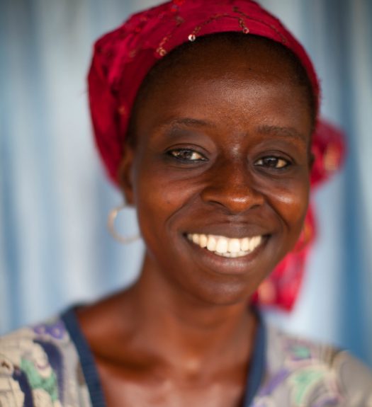 Female cocoa farmer from Cote d'Ivore smiles, wearing colorful clothing.