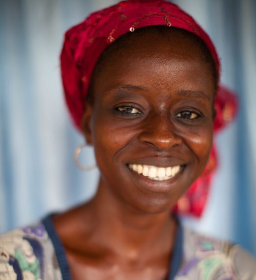 Female cocoa farmer from Cote d'Ivore smiles, wearing colorful clothing.