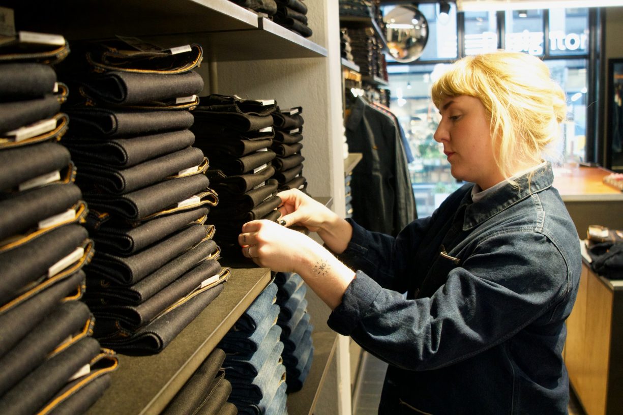 Store worker at Nudie Jeans organizes a stack of denim.