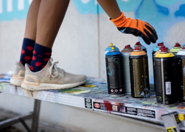 Artist, J Muzacz standing on ladder reaching down for spray paint.