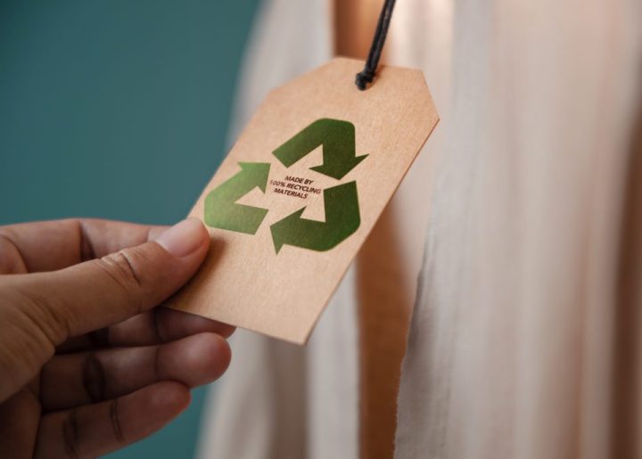 A person's hand holds the corner of a tag with the recycle sign on it.
