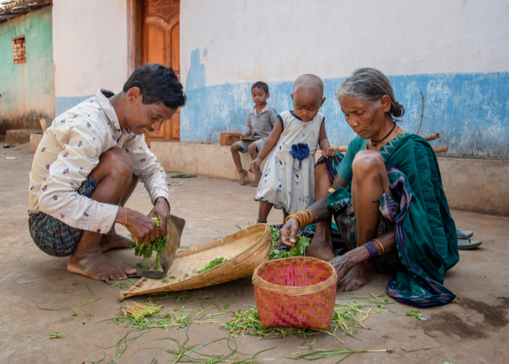 Lingra Raj Nag and his mother work outside processing vegetables and placing them in woven baskets. Nearby are Lingra Raj’s two young children.