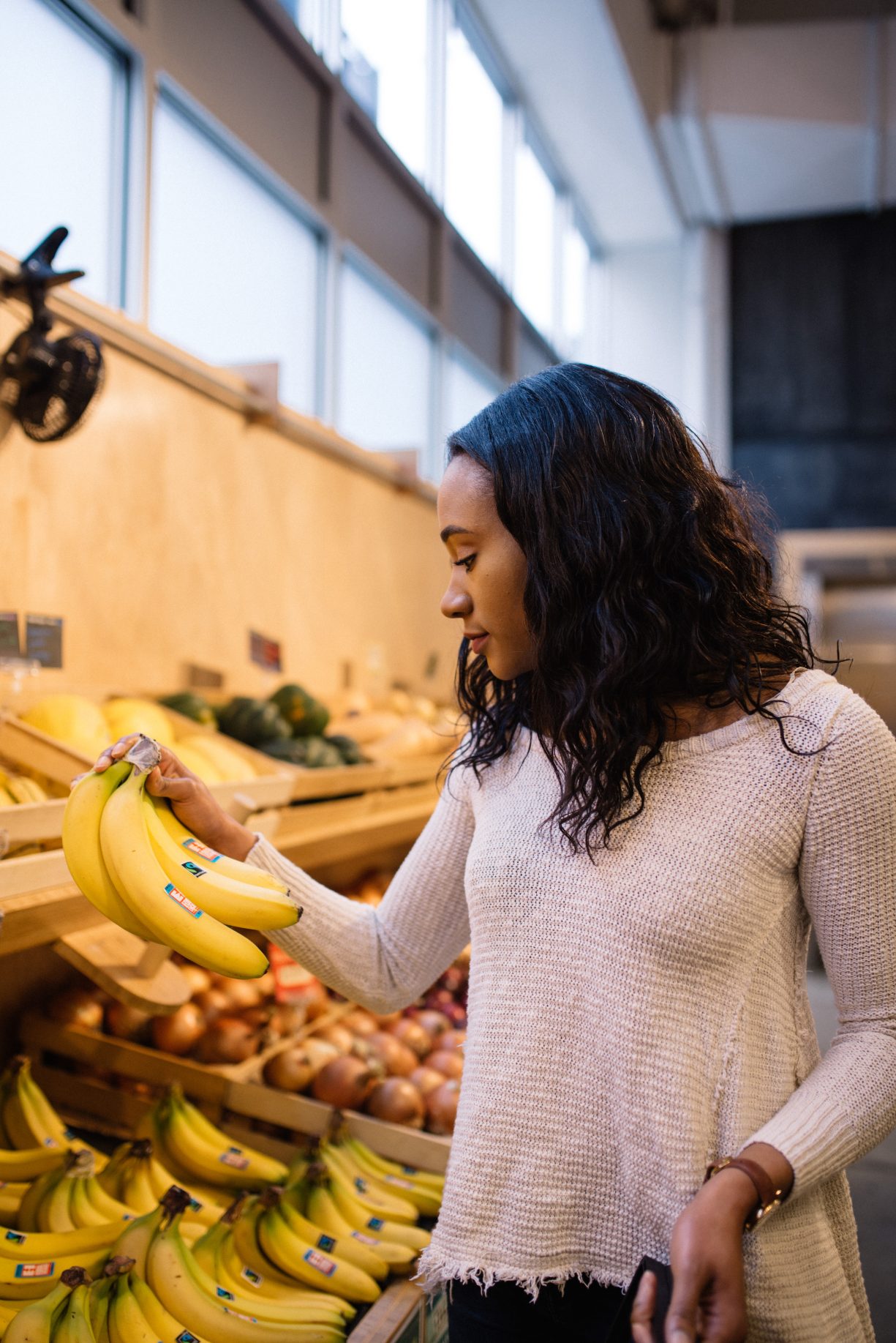 Young woman in grocery store examines a bunch of ripe bananas.